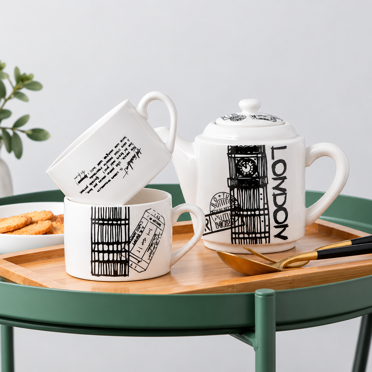 White ceramic tea set with black London-themed illustrations and text, including a teapot, mug, and smaller cup, arranged on a wooden tray over a green table.