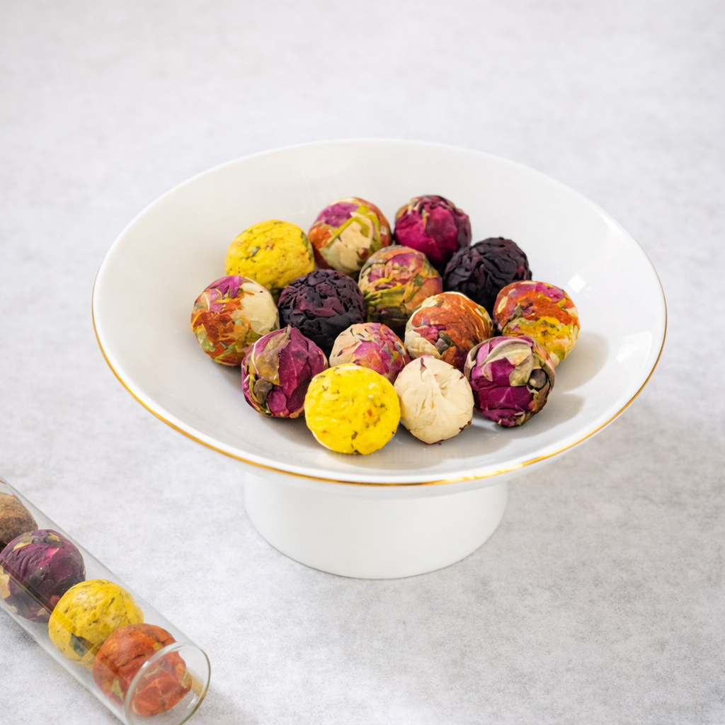 Colorful dried flower tea balls in a white bowl on a light gray background
