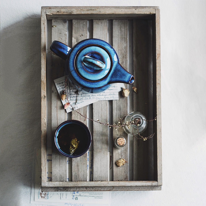 Blue ceramic teapot and cup on a wooden tray with a white background