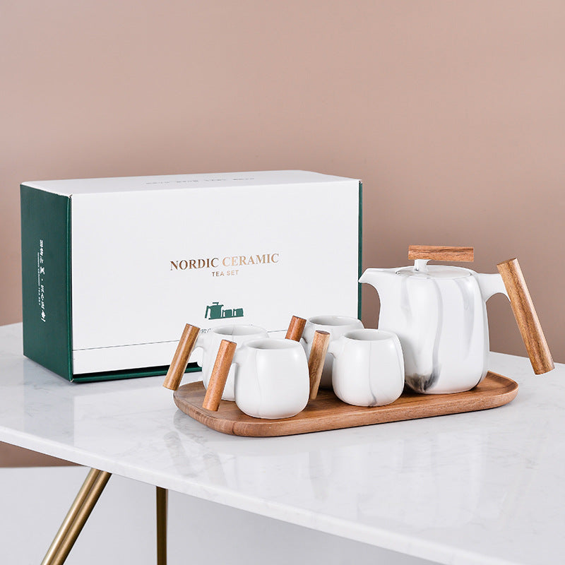 Nordic ceramic tea set with a teapot, cups, and a wooden tray on a white surface.