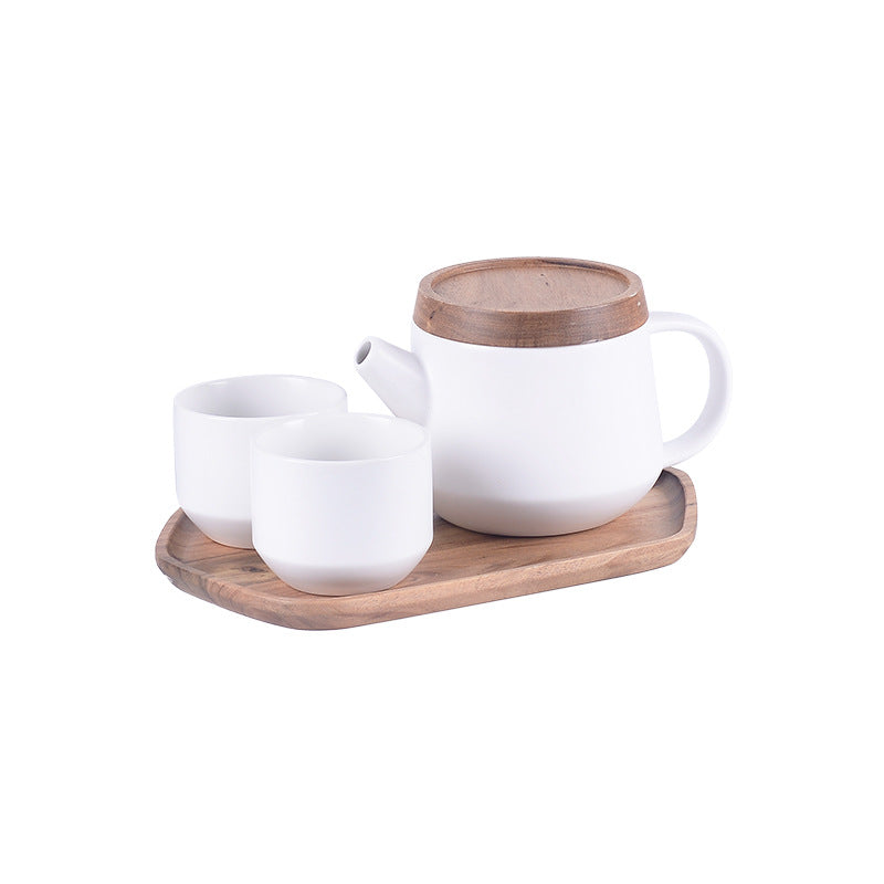 A white ceramic teapot and two matching cups with light brown wooden lids and a matching wooden tray, set against a plain white background.