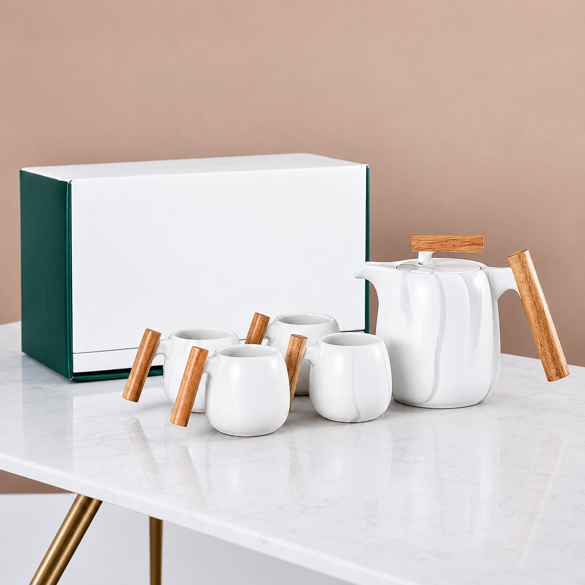 White ceramic tea set with light wood handles and lids, arranged on a white marble table next to a white and dark green gift box against a beige background.