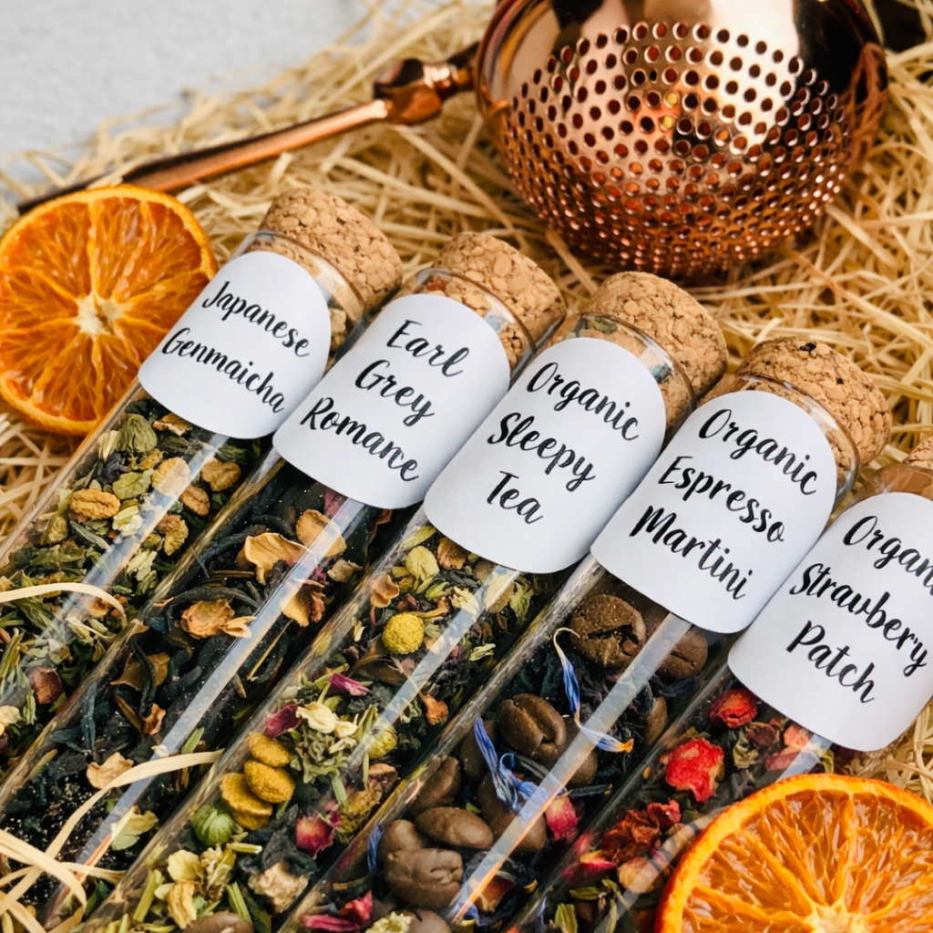 Tea bags in test tubes with labels on a bed of hay and dried oranges.