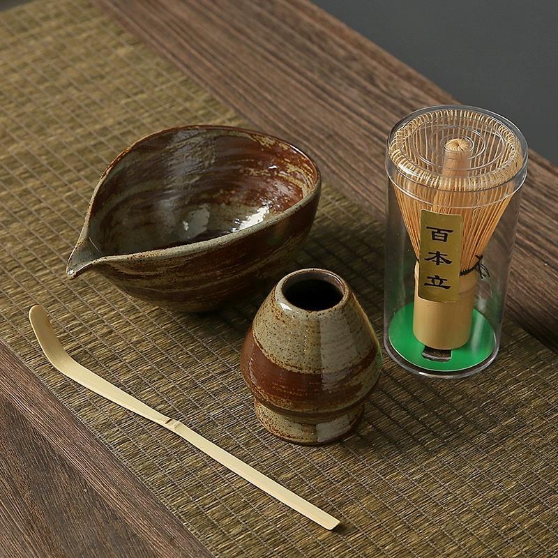 Tea-making set with ceramic bowl, whisk, and other tools on a wooden surface.