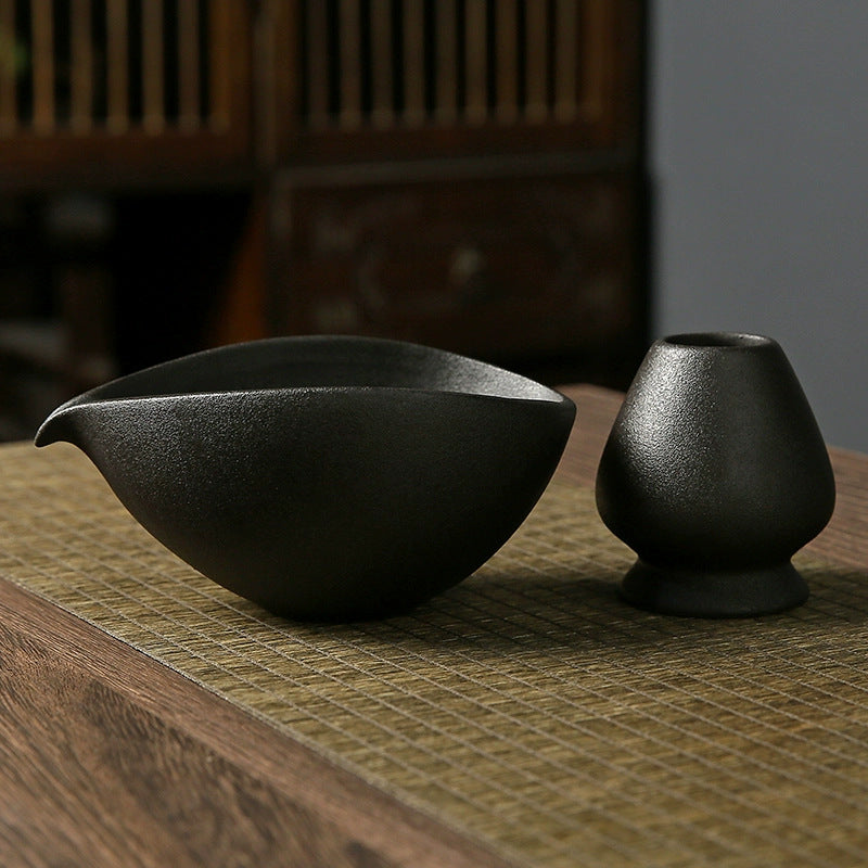 Two black ceramic teapots on a textured surface with a blurred background