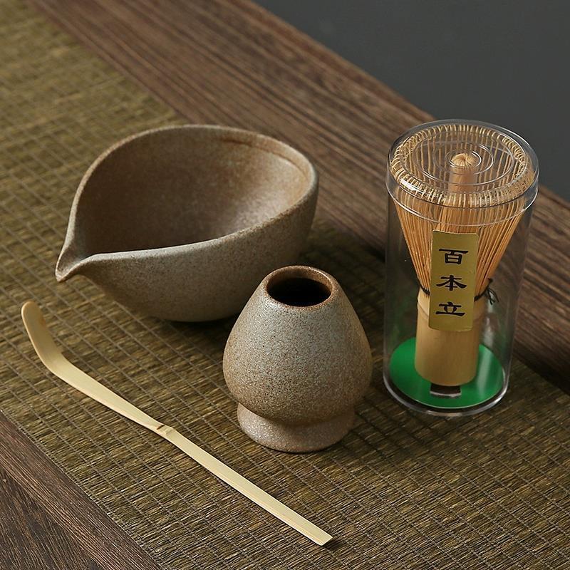 Tea-making set with a bowl, whisk, and container on a wooden surface.