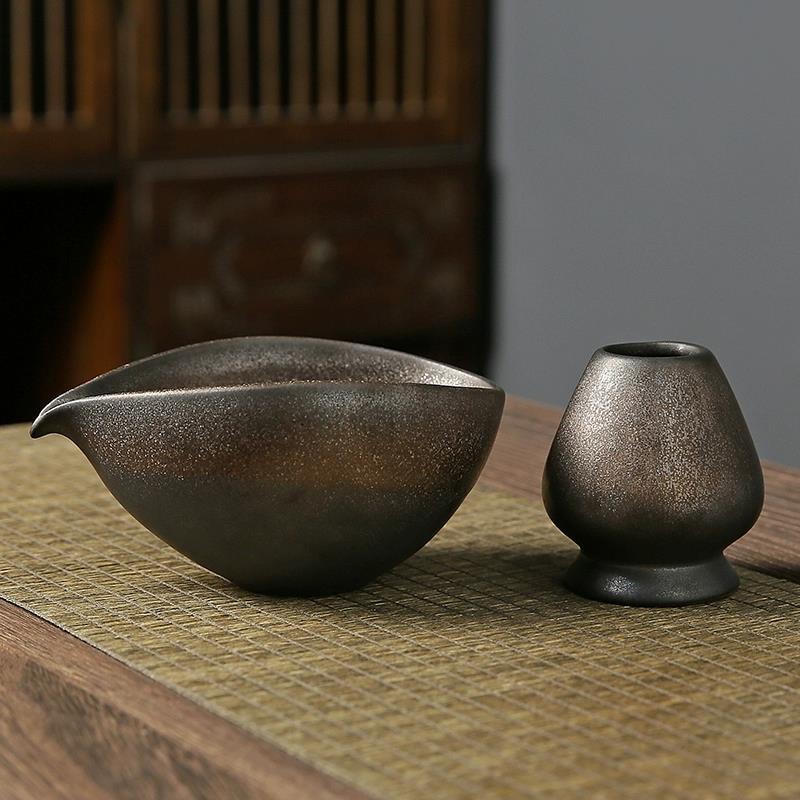 Two dark brown ceramic vessels on a textured surface with a blurred background