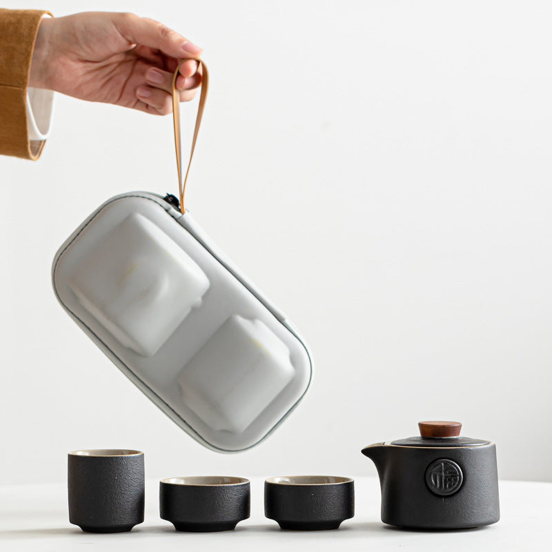 Set of black ceramic tea cups and teapot with a gray carrying case on a white background