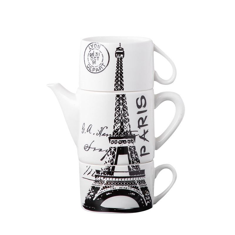 A stack of three white ceramic mugs with black Eiffel Tower illustrations and French script, featuring a postmark design on the top mug.