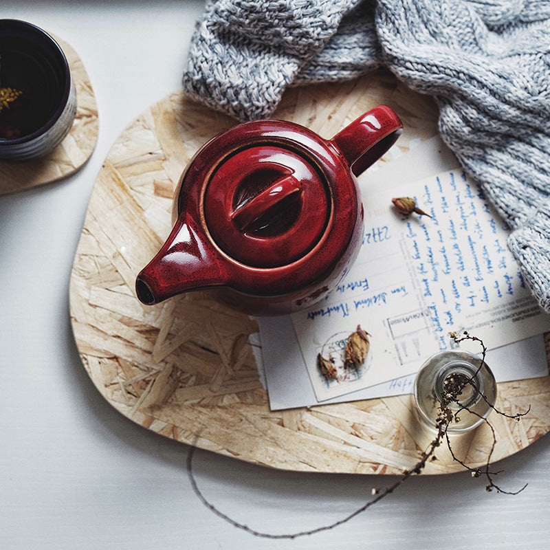 Red teapot on a wooden tray with a cup, scarf, and notes on a white surface